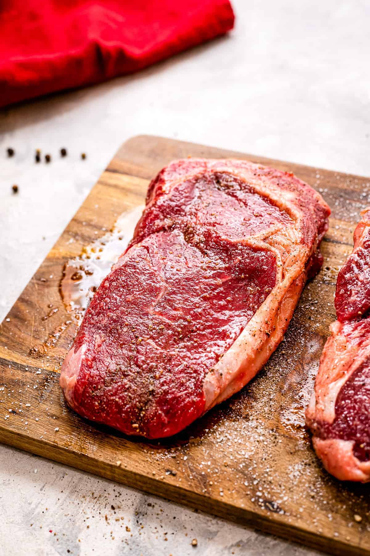 Wood cutting board with raw steak seasoned with salt and pepper