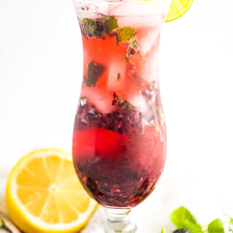 A tall glass with a blackberry mojito garnish with lime