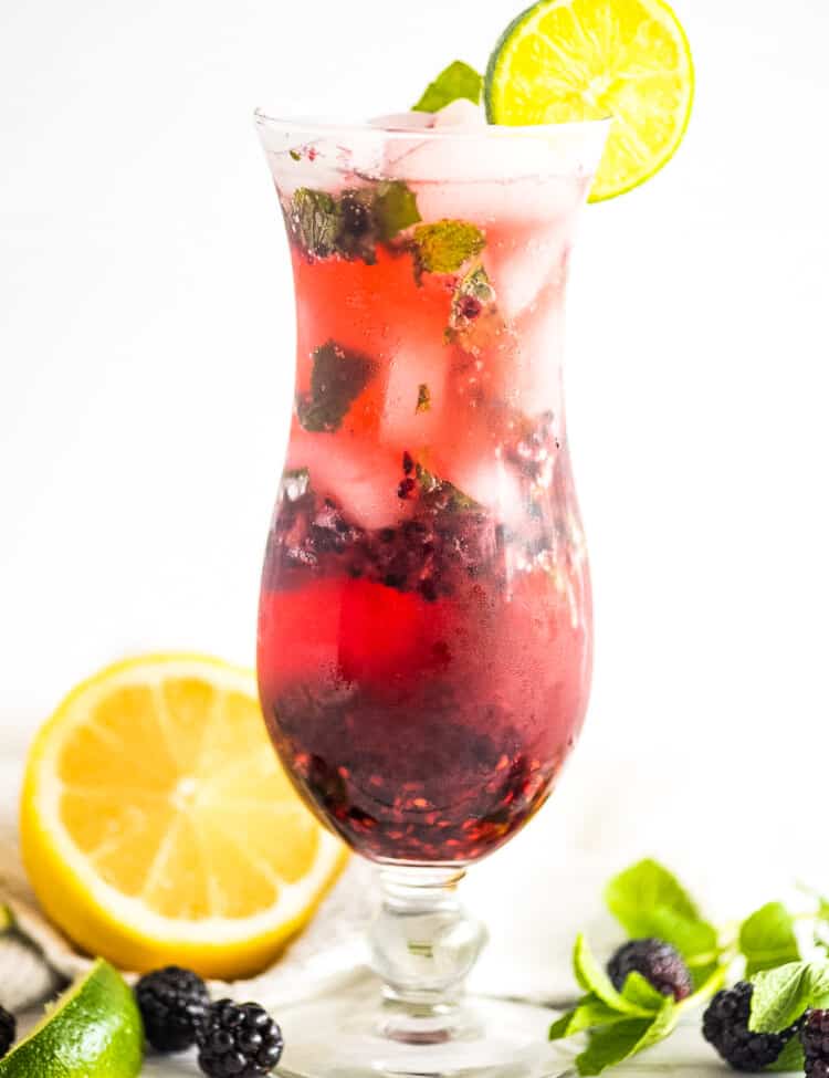 A tall glass with a blackberry mojito garnish with lime