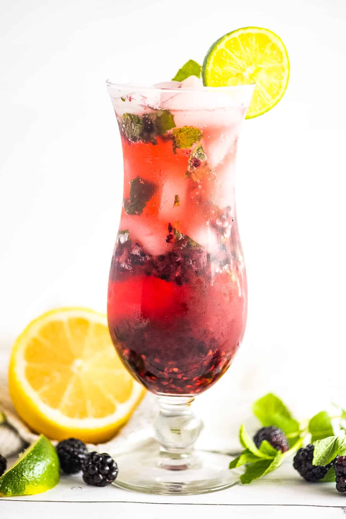 A tall glass with a blackberry mojito garnish with lime