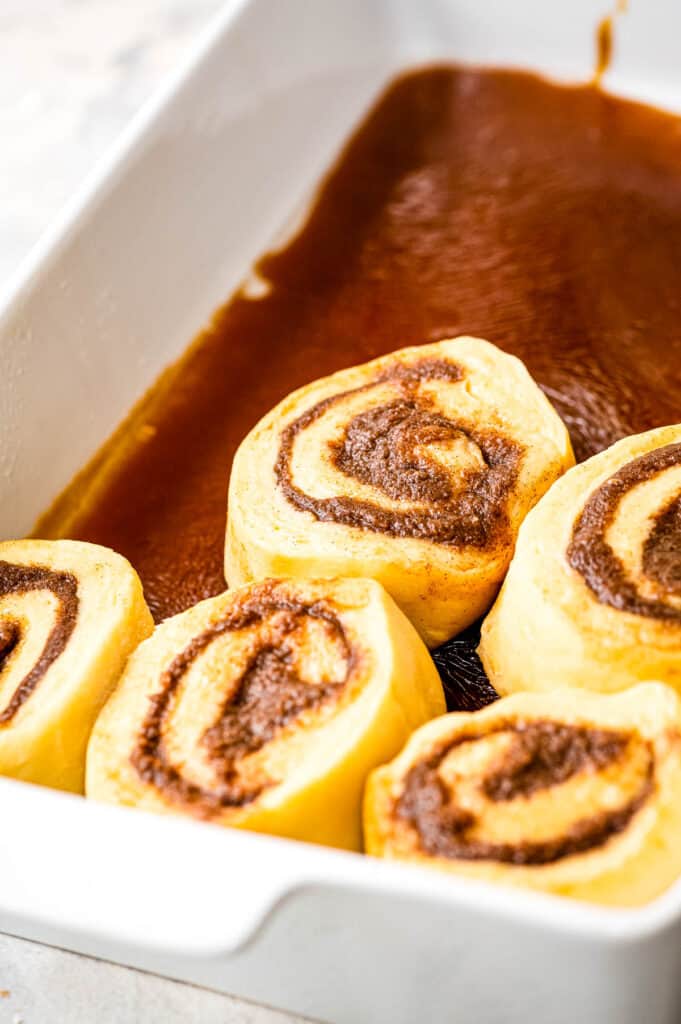 White baking dish with caramel filling on bottom and raw rolls on top