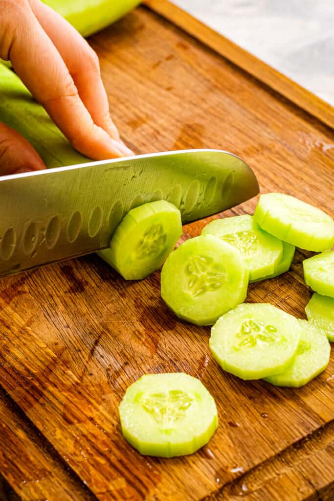 Chef knife slicing a cucumber thinly