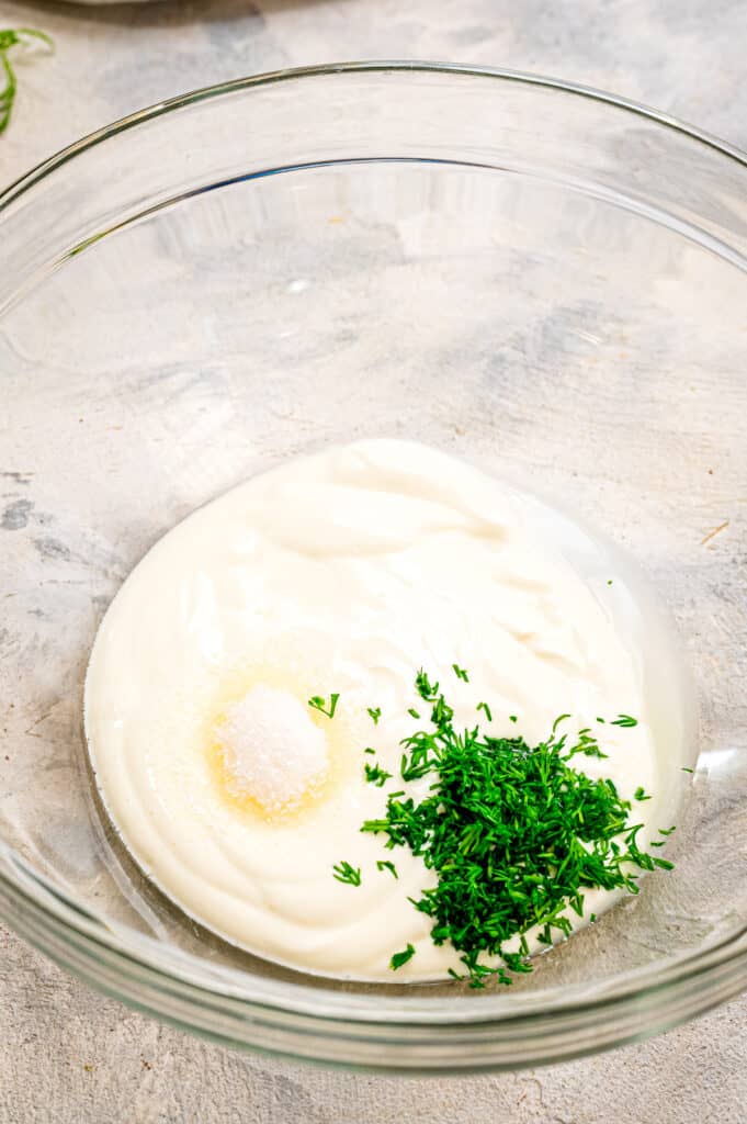Glass bowl with ingredients to make sour cream dill sauce