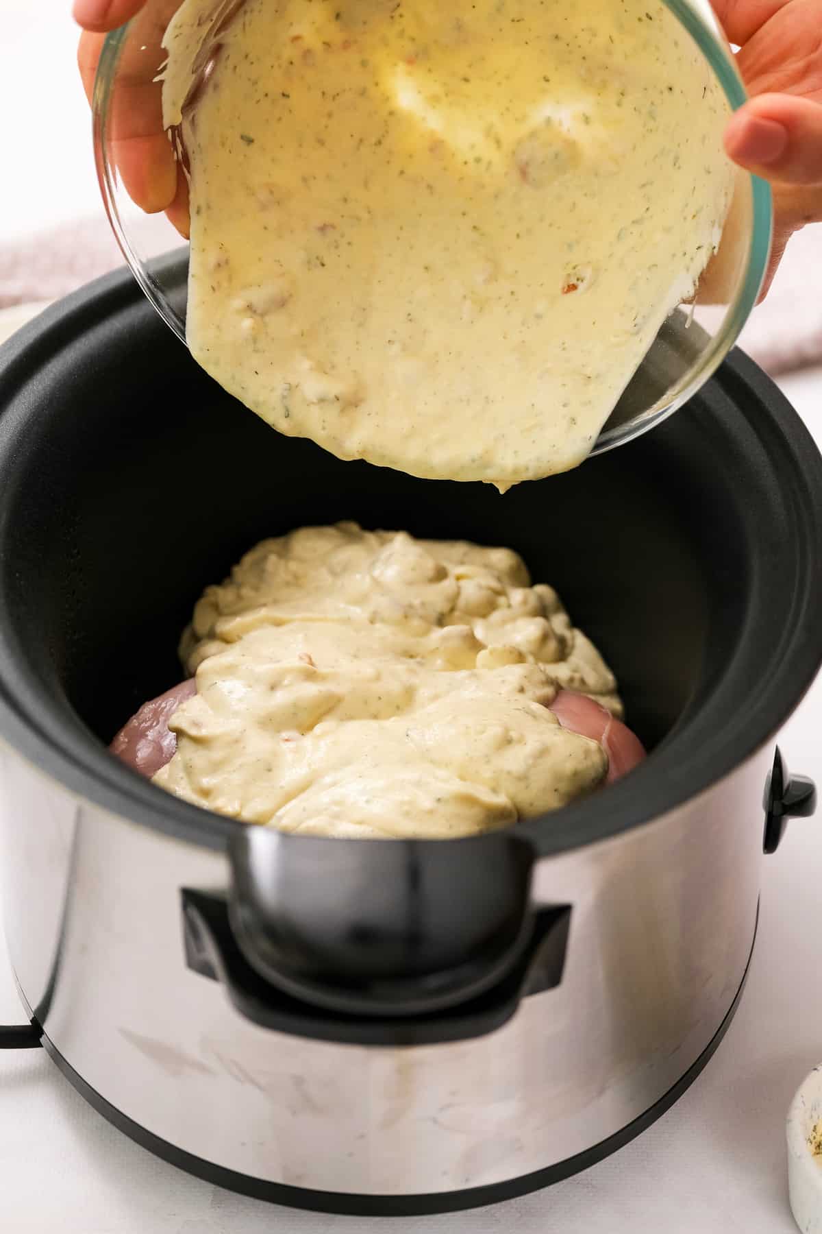 Pouring cream sauce over chicken breasts in slow cooker