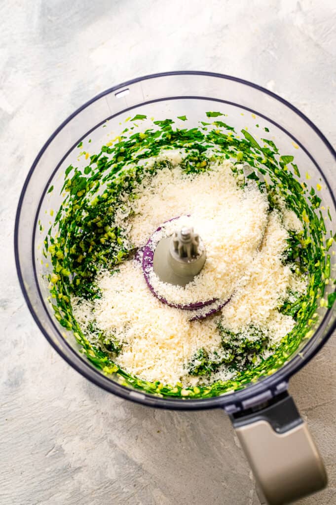 Food processor with pesto blended and parmesan cheese on top