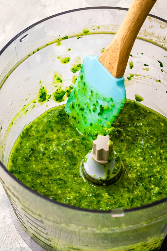 A food processor with pesto in it and spatula stirring it