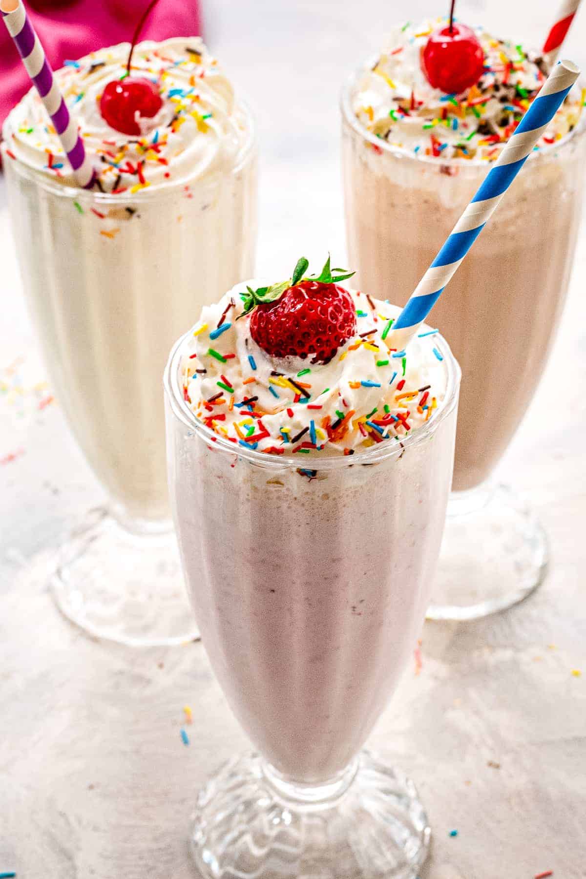 Vanilla, strawberry and chocolate milkshakes with whipped cream and sprinkles