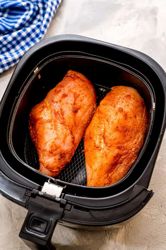 Raw chicken breasts in air fryer basket