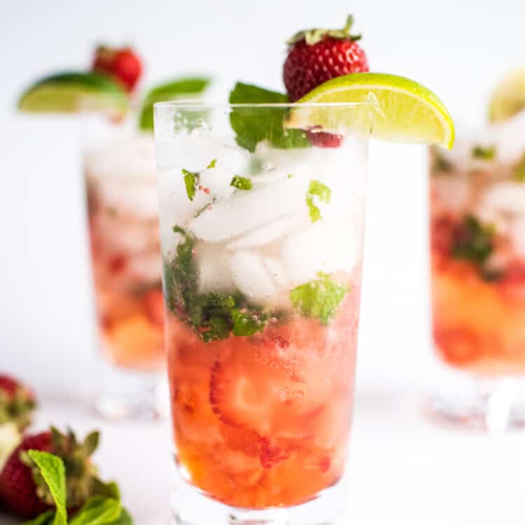 Tall glass with strawberry mojito garnished with lime and strawberry