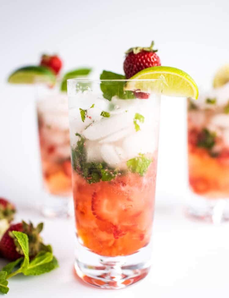 Tall glass with strawberry mojito garnished with lime and strawberry