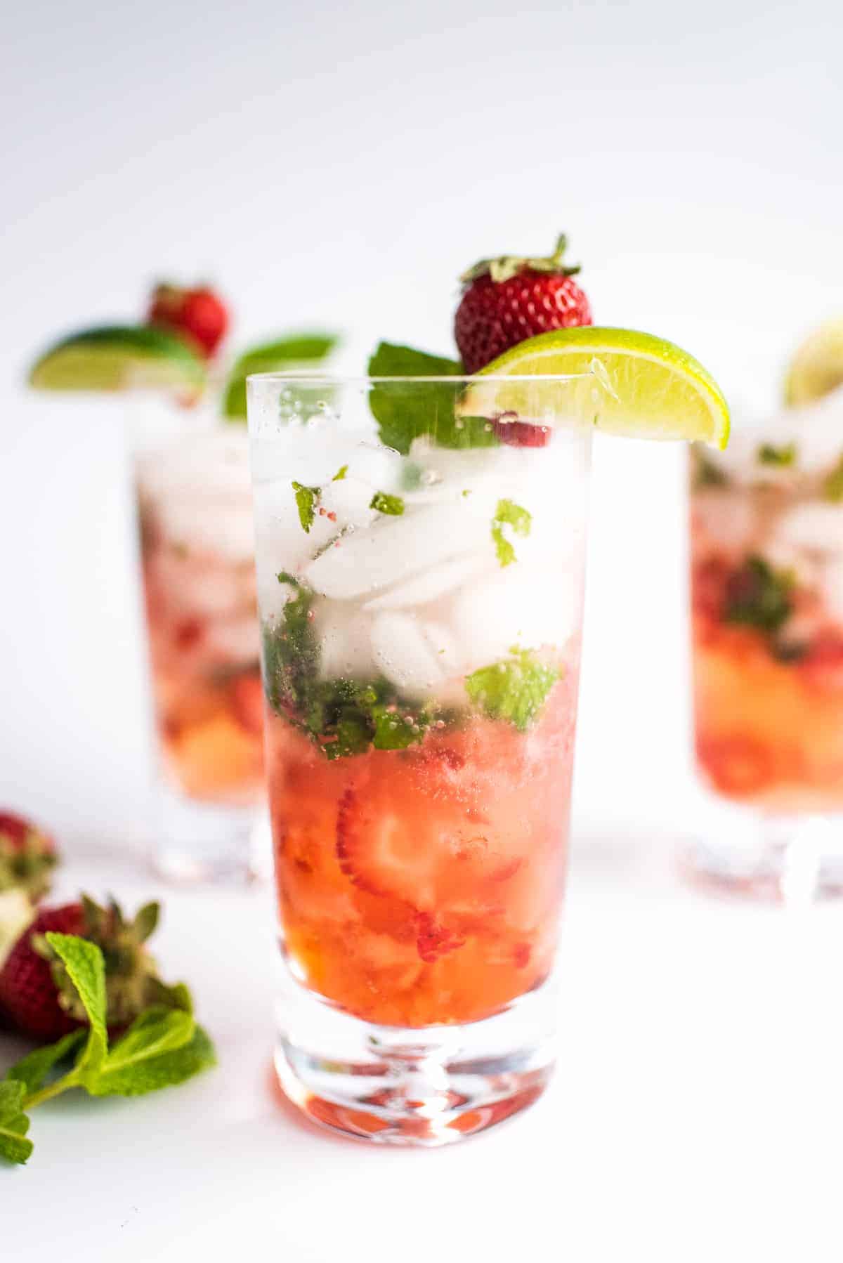 Tall glass with strawberry mojito garnished with lime and strawberry