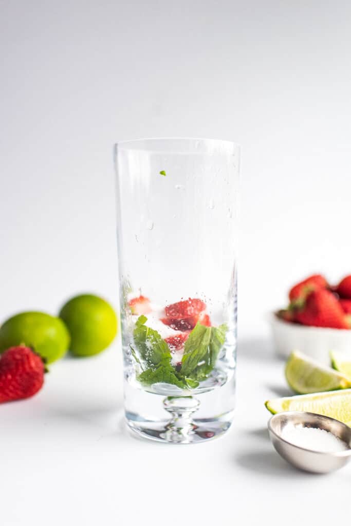 Tall glass with ingredients to muddle for strawberry mojito