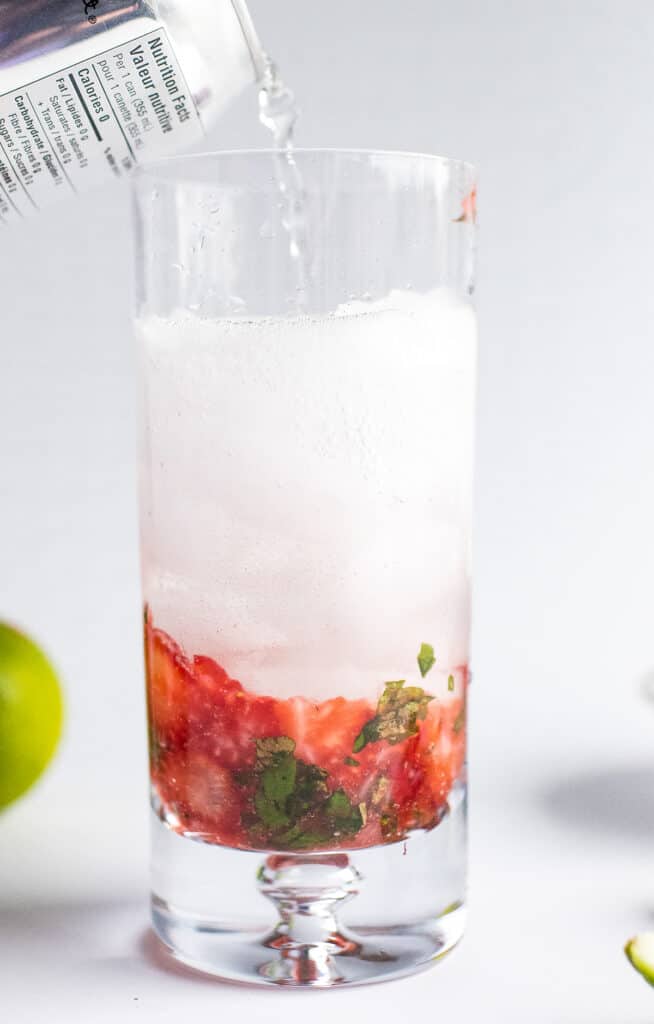 Pouring club soda into tall glass with mojito and ice