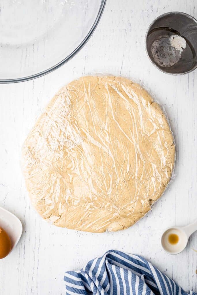 Sugar Cookie dough in round slab with plastic wrap over it