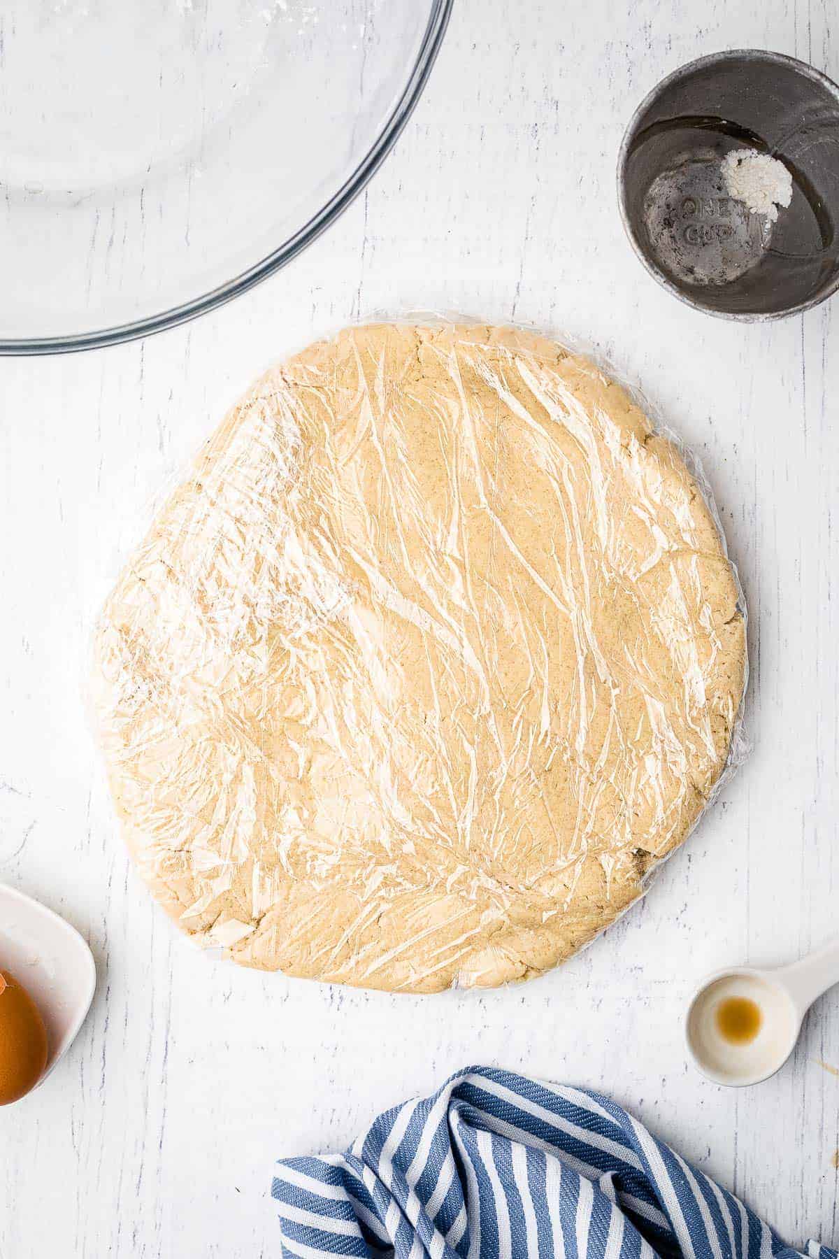 Sugar Cookie dough in round slab with plastic wrap over it