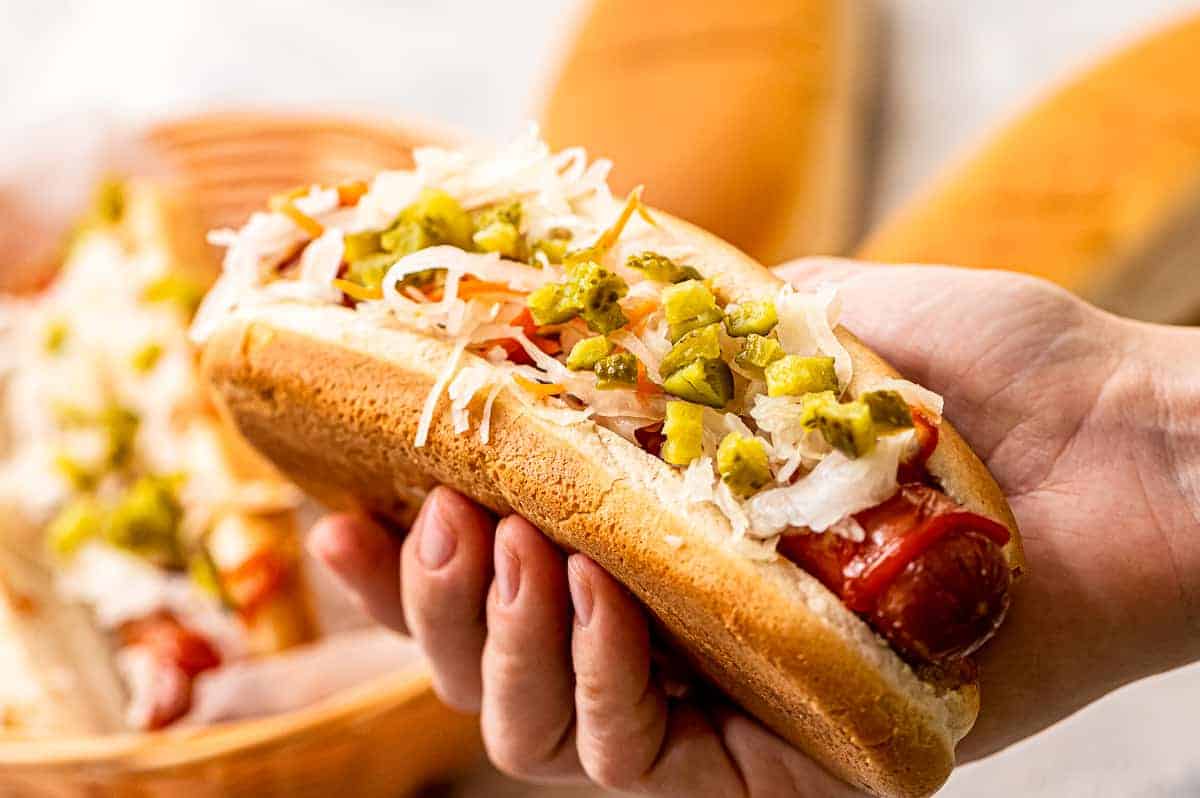 Hand holding hot dog in a bun with toppings