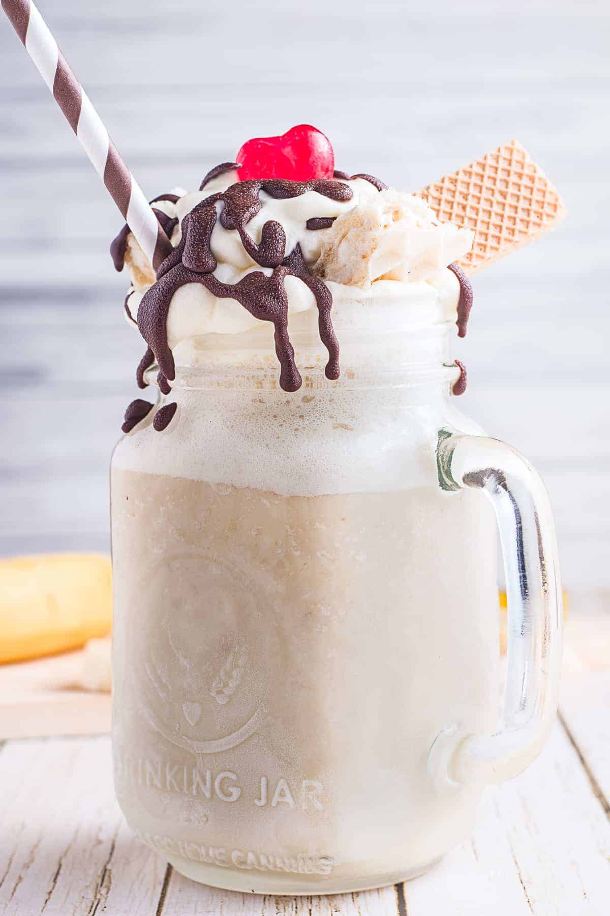 Banana Milkshake in a mason jar topped with chocolate syrup, maraschino cherry and wafer