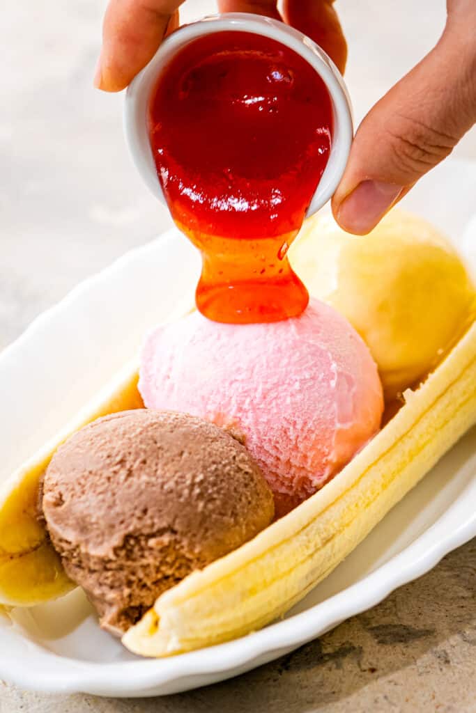 Pouring strawberry syrup on top of strawberry ice cream scoop