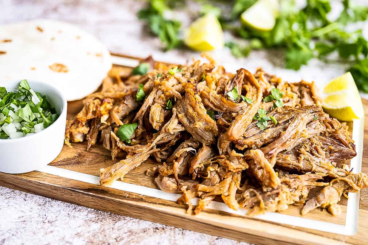 Shredded pork carnita meat on platter with tortillas and cilantro