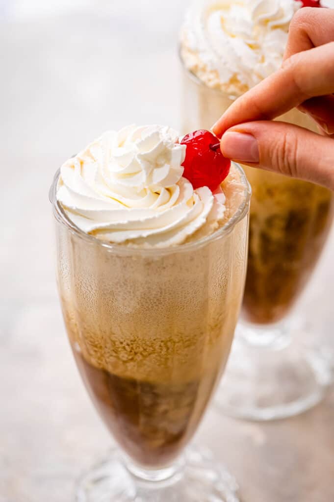 Hand placing maraschino cherry on top of whipped cream on root beer float