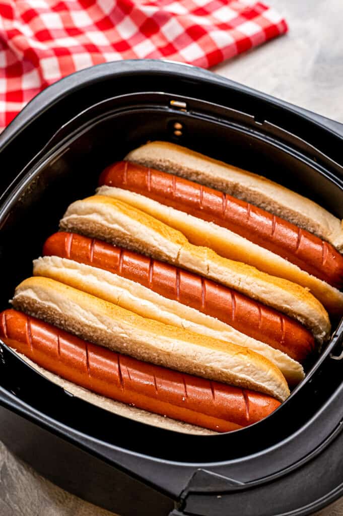 Air Fryer basket with hot dogs inside of buns