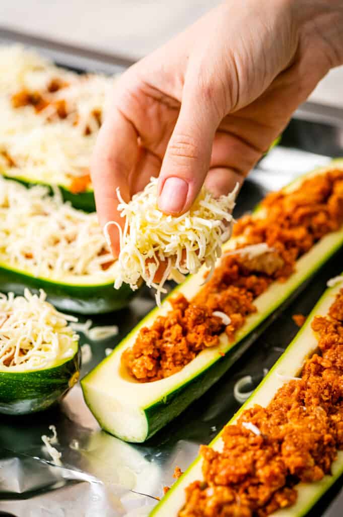 Hand sprinkling Mozzarella cheese over the top of zucchini boats