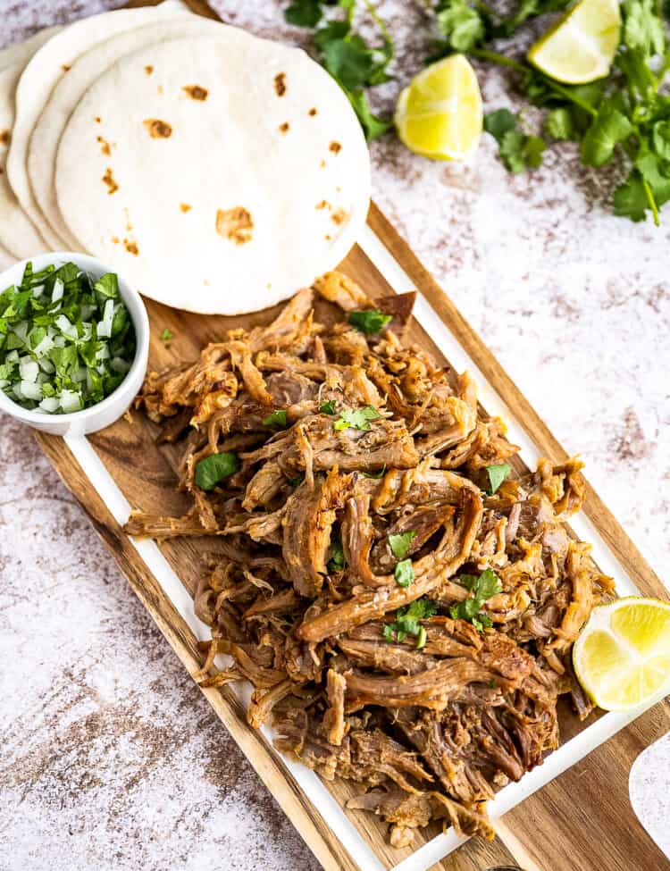 Overhead image of carnita meat on platter with tortillas