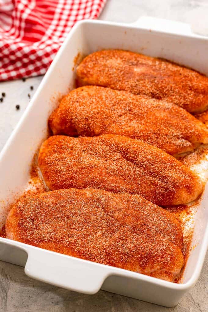 White baking dish with seasoned chicken breasts in it