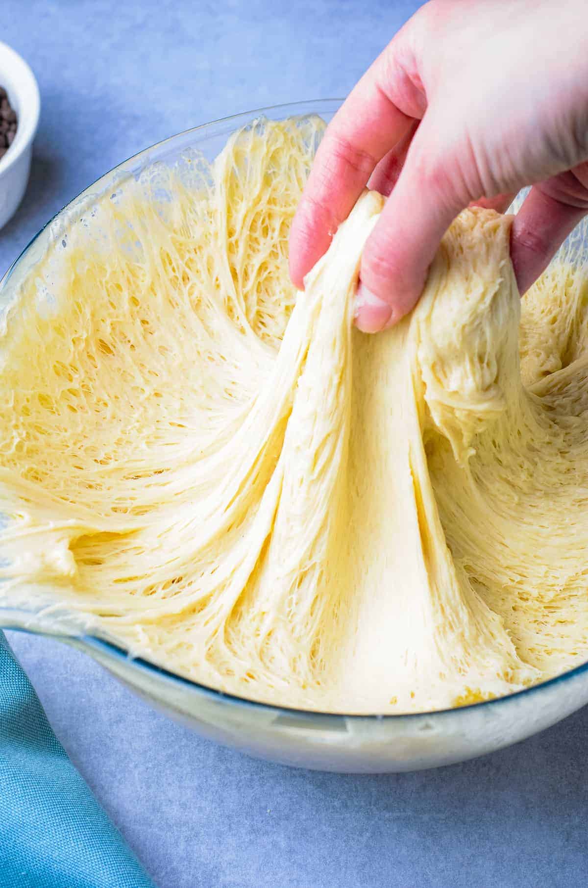 Hand pulling donut dough in glass bowl