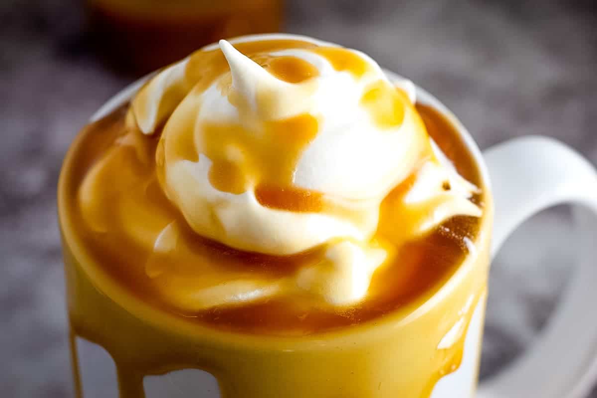 Close up image of a white coffee mug with whipped cream and caramel on top