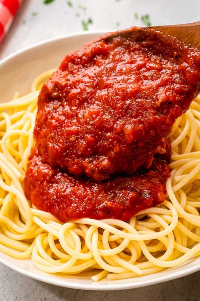 Spoon putting spaghetti sauce on a bed of spaghetti noodles