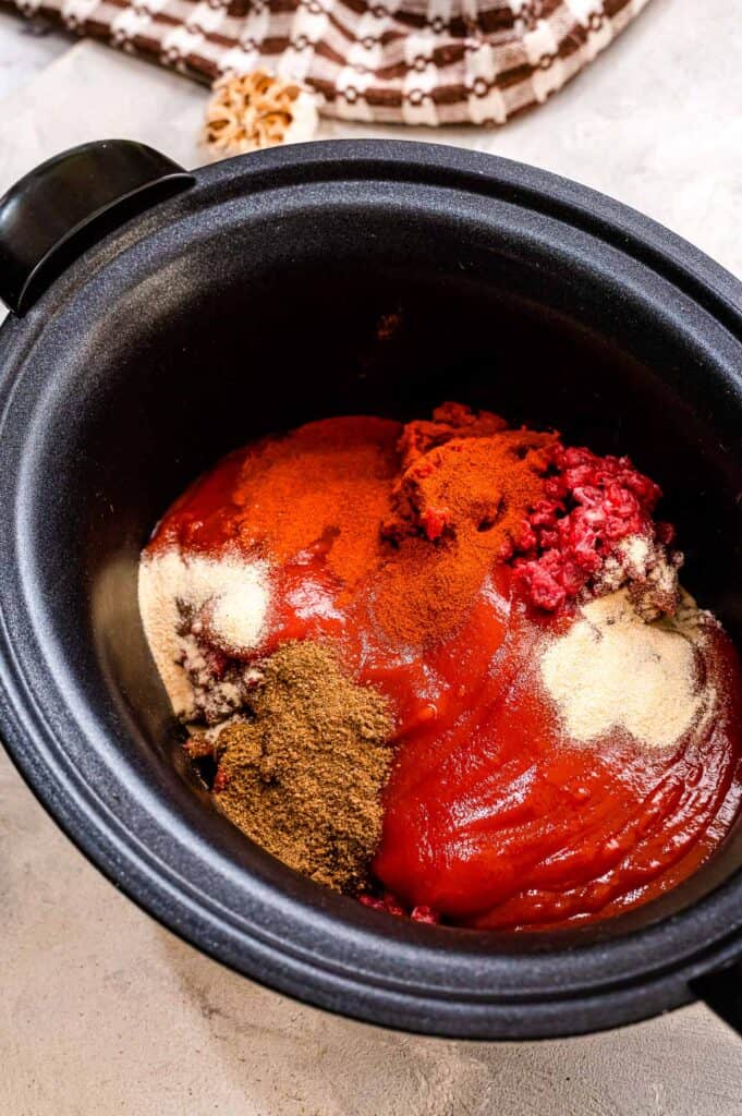 Black crock pot with ground beef, tomato sauce and spices