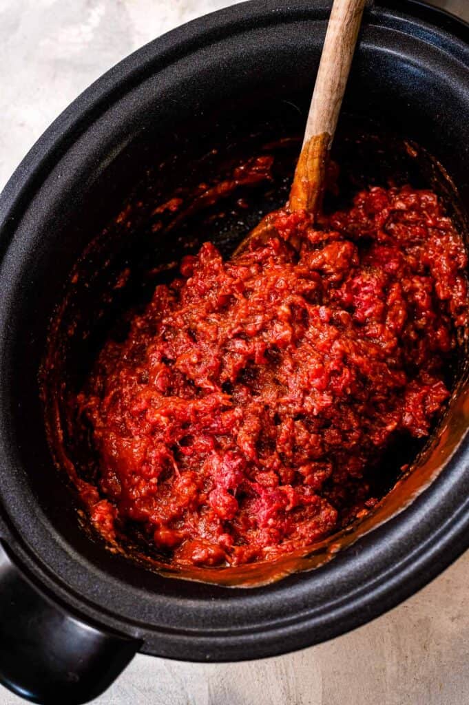 Black crock pot with ground beef, tomato sauce and spices mixed together