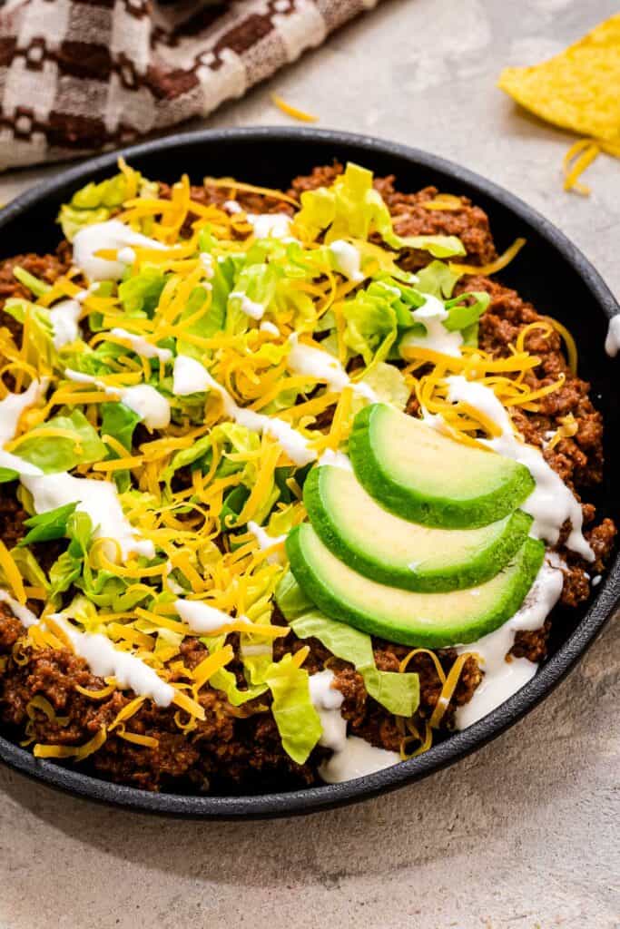 Small cast iron skillet with taco meat topped with lettuce, sour cream and avocado