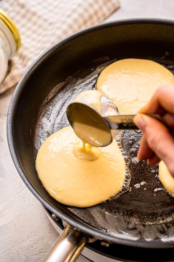 Hand pouring pancake batter our of a measuring cup