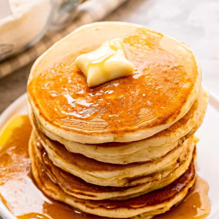 Stack of pancakes with butter and syrup on white plate