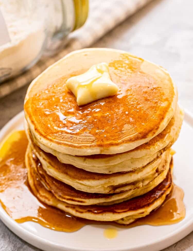 Stack of pancakes with butter and syrup on white plate