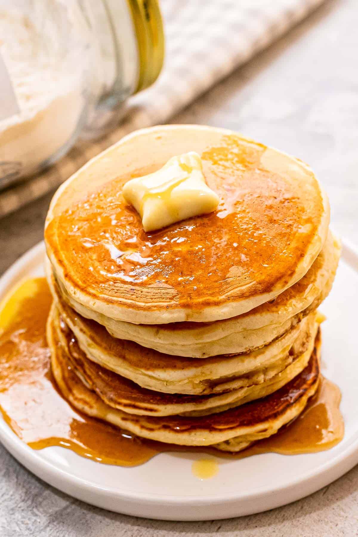 Stack of pancakes with butter and syrup on white plate