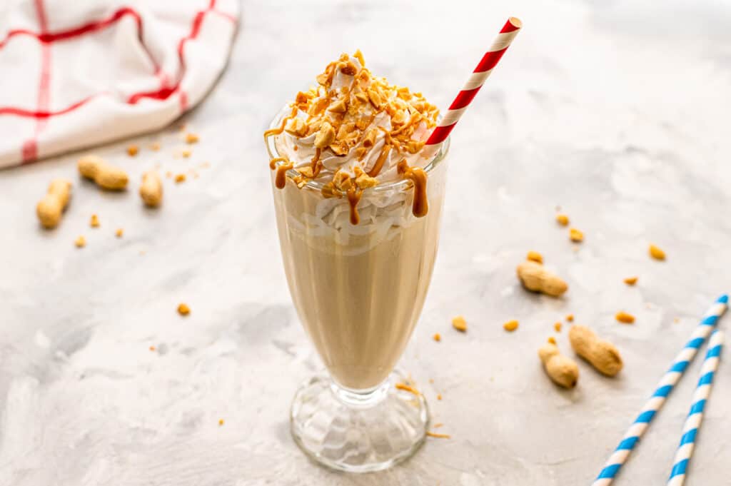 Peanut Butter Milkshake in a tall glass with chopped peanuts, whipped cream and drizzled peanut butter