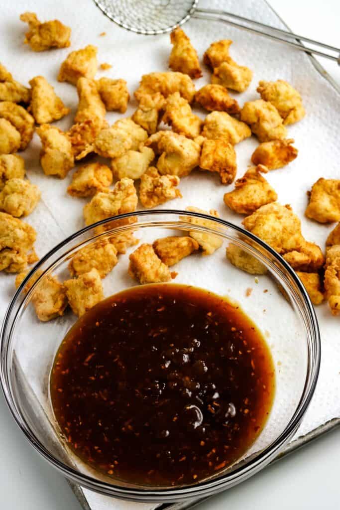 Orange sauce in bowl with fried chicken pieces behind it on baking sheet