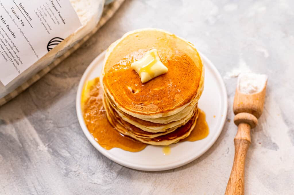 White plate with stack of pancakes topped with butter and syrup