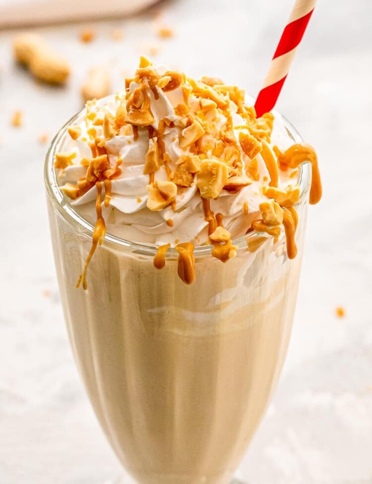 Tall glass with peanut butter milkshake with whipped cream and chopped peanuts