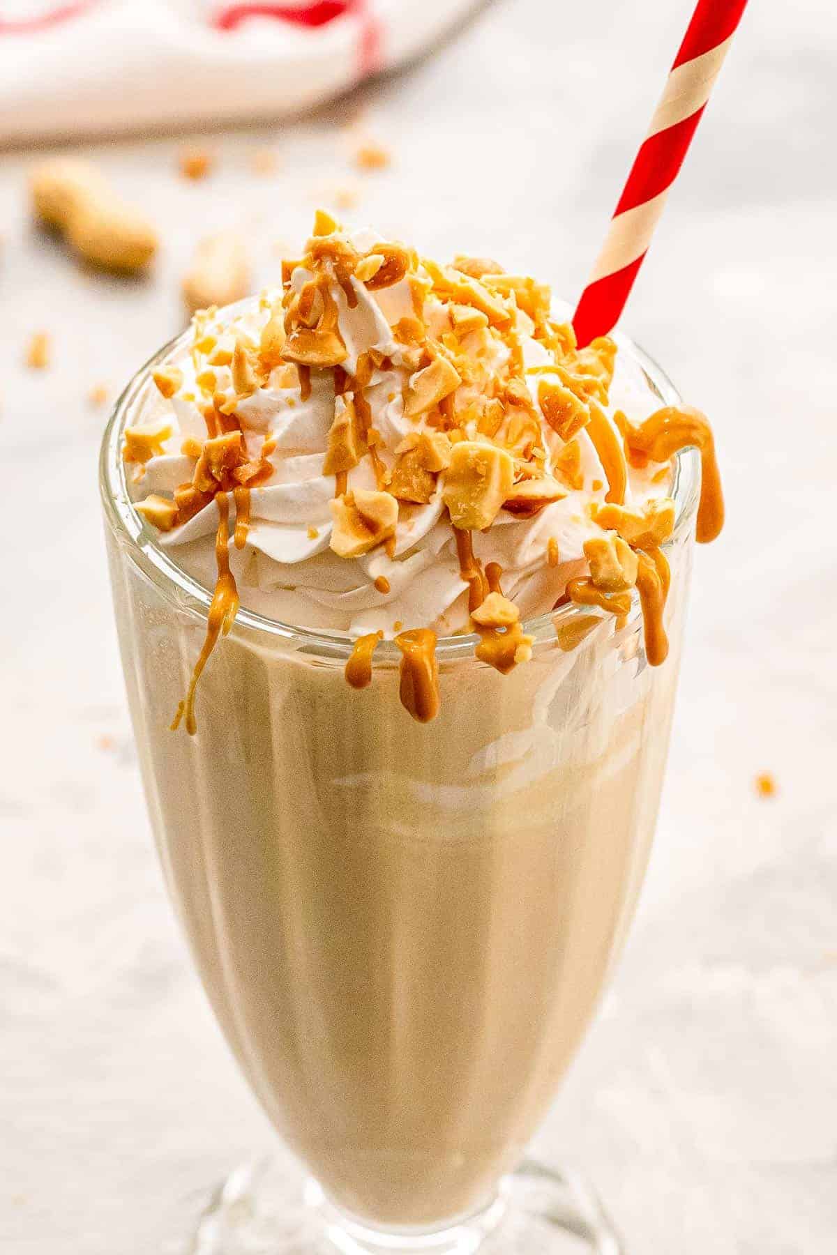 Tall glass with peanut butter milkshake with whipped cream and chopped peanuts