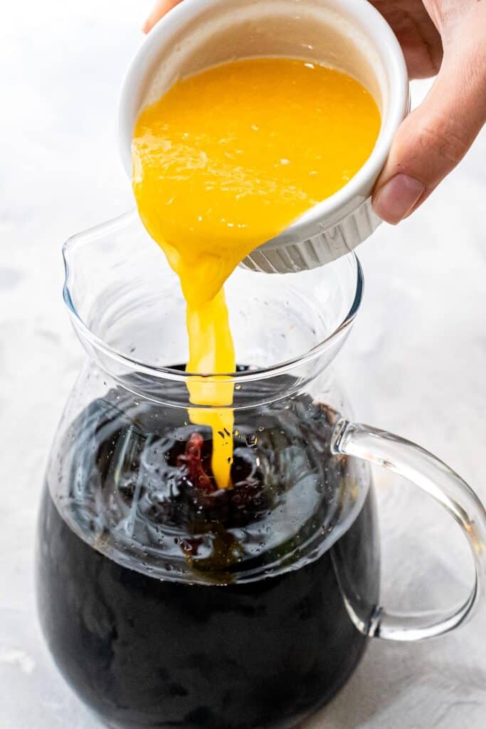 Hand pouring orange juice into red sangria