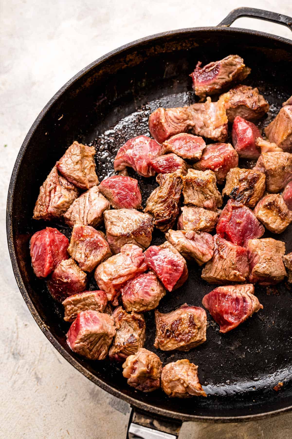 Browning pieces of steak in cast iron skillet