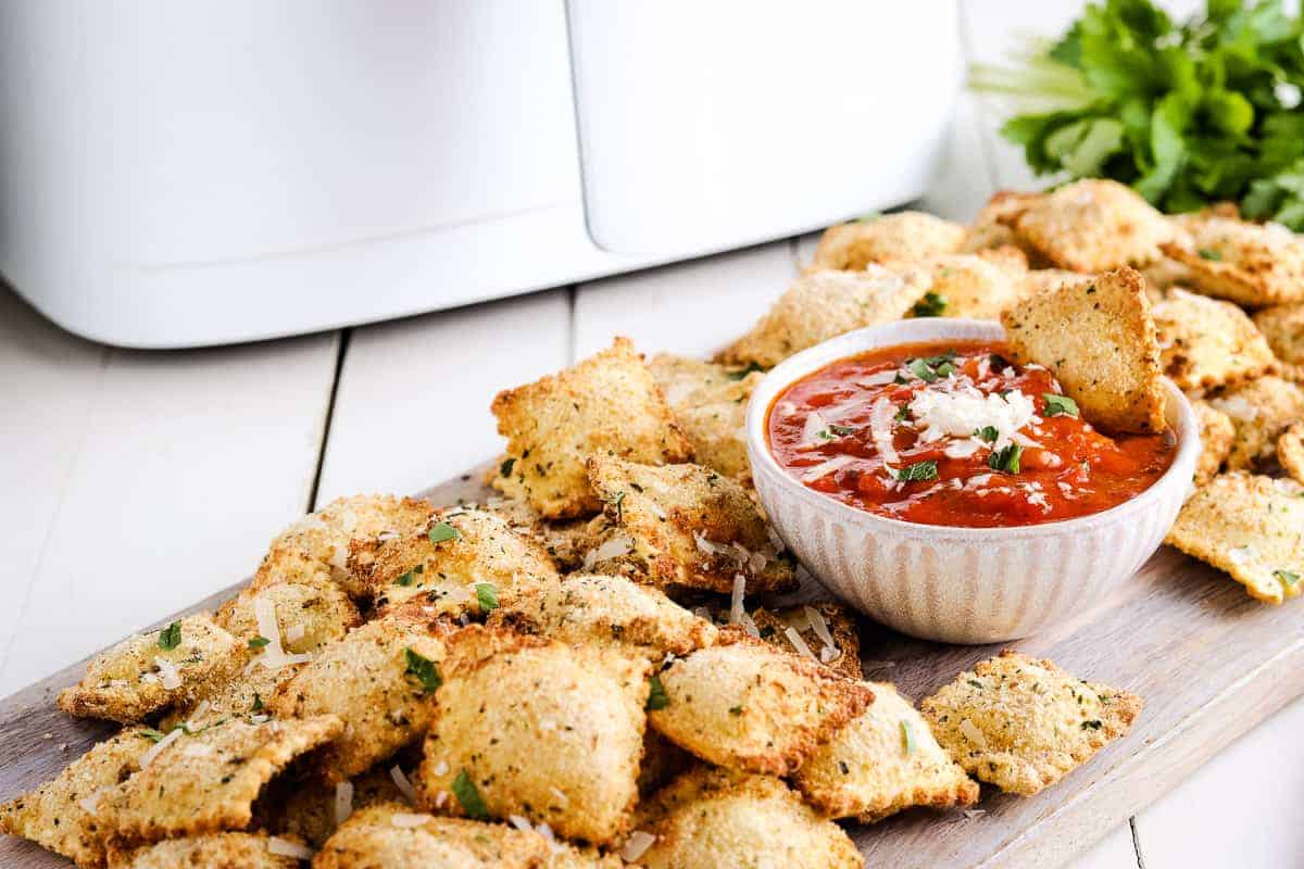 Toasted Air Fryer Ravioli on board with a bowl of marinara sauce