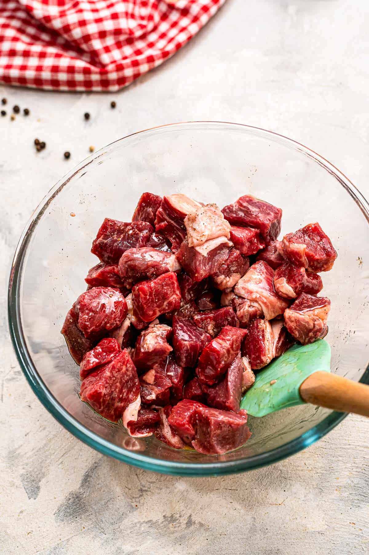 Glass bowl stirring steak pieces, olive oil, salt and pepper together