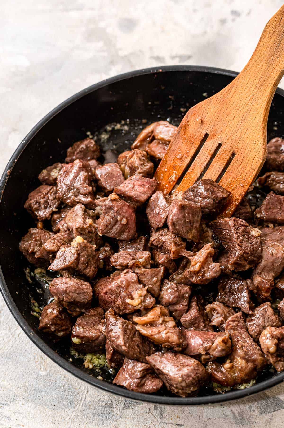 Spatula tossing steak bites in garlic butter in a skillet