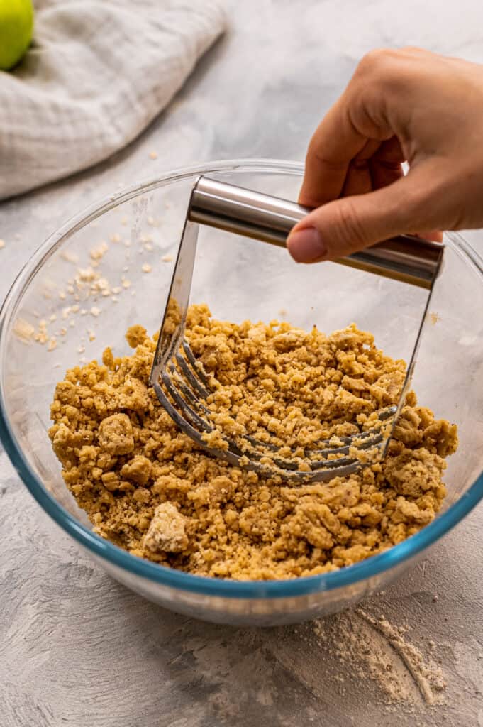 Hand cutting butter into streusel topping in glass bowl with pastry cutter.