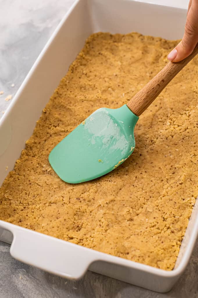 Spatula pressing shortbread crust into rectangle baking dish